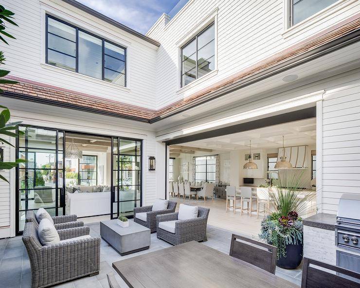 Gray wicker patio chairs facing each other finished with a rectangular concrete coffee table in the center for a symmetrical design. Concrete pavers bring a modern finish to the patio design complementing the neutral finishings.