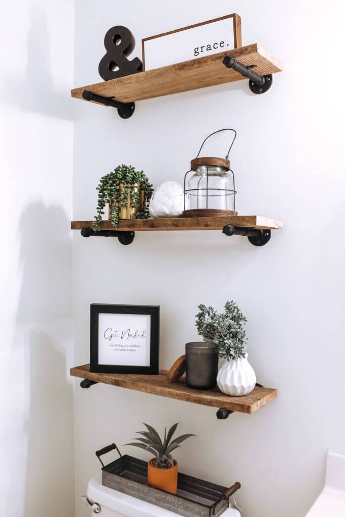 wood open shelving on wrought iron pipes decorated in farmhouse style over toilet
