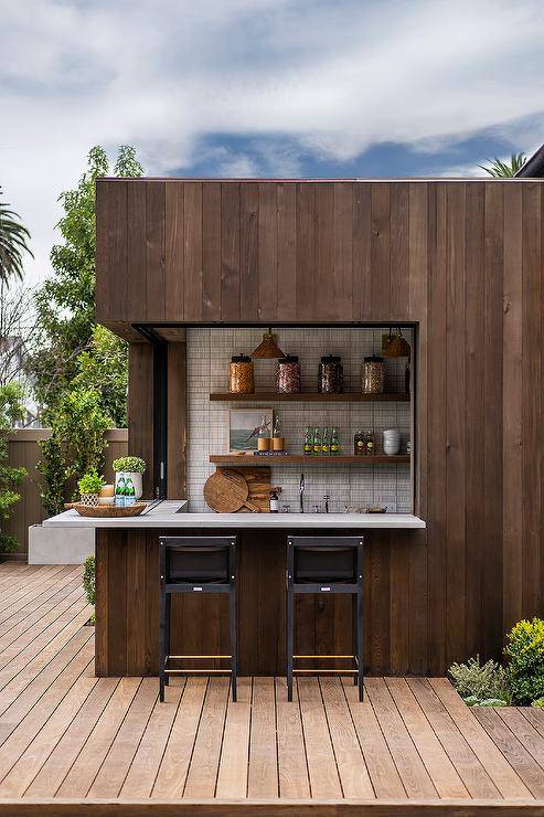 Black stools sit on a brown plank deck at an l-shaped brown plank wet bar accented with concrete countertops.