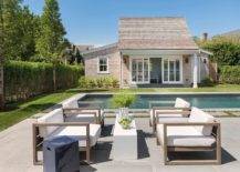 Beside an in ground swimming pool lined with concrete pavers, Restoration Hardware Aegean Teak Chairs sit on a concrete floor at a slim white coffee table accented with a black end table.