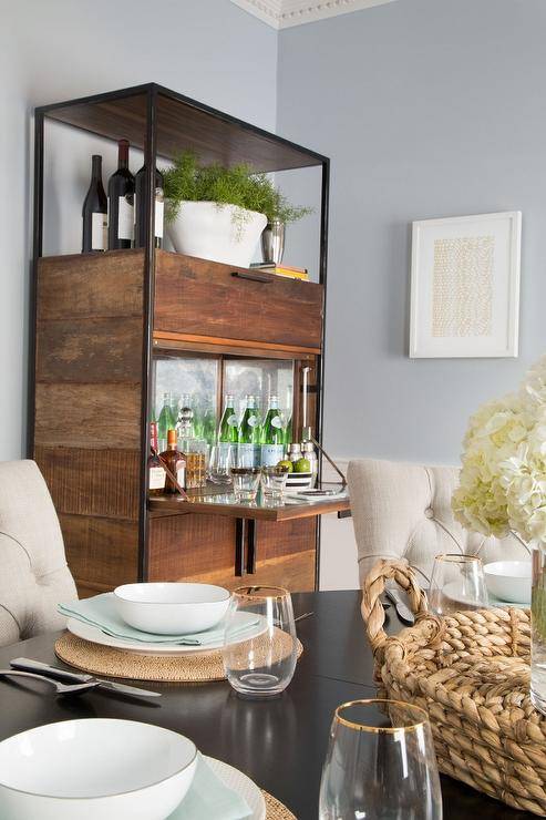 Beautiful dining room features a dark stained oval dining table lined with beige tufted dining chairs placed in front of a metal and wood industrial bar cabinet with fold down table and mirrored backsplash.