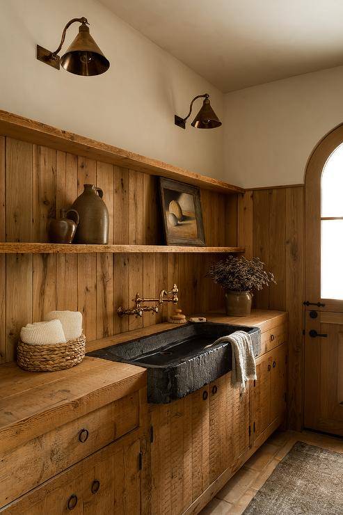 Rustic cottage kitchen features a black stone trough sink with an aged brass vintage style faucet and rustic wooden cabinets.