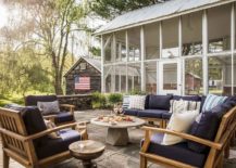 Country style farmhouse patio features a teak outdoor sofa with navy blue cushions and a round concrete pedestal coffee table.