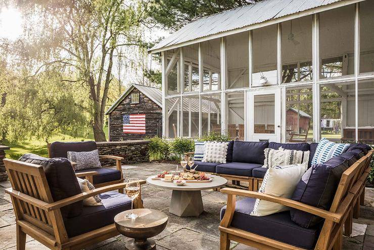 Country style farmhouse patio features a teak outdoor sofa with navy blue cushions and a round concrete pedestal coffee table.