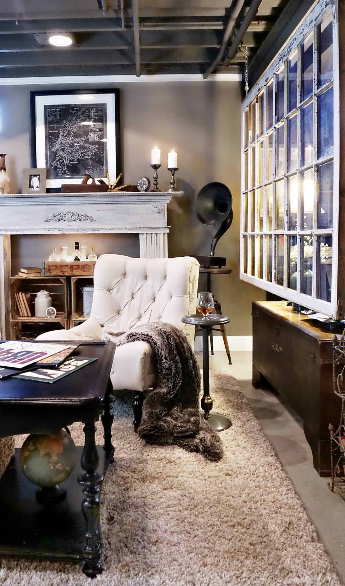 rustic industrial styled basement with dark grey walls white tufted sitting chair faux fur throw salvaged window divider