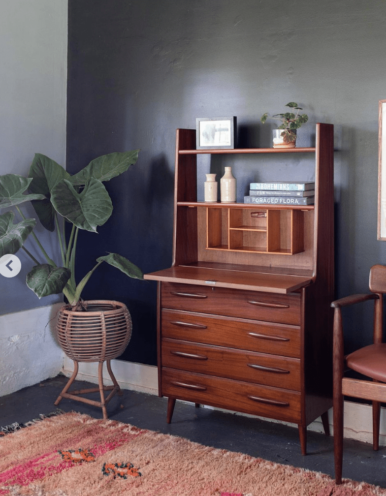 mid century modern fold down desk in black painted room with plant and boho rug