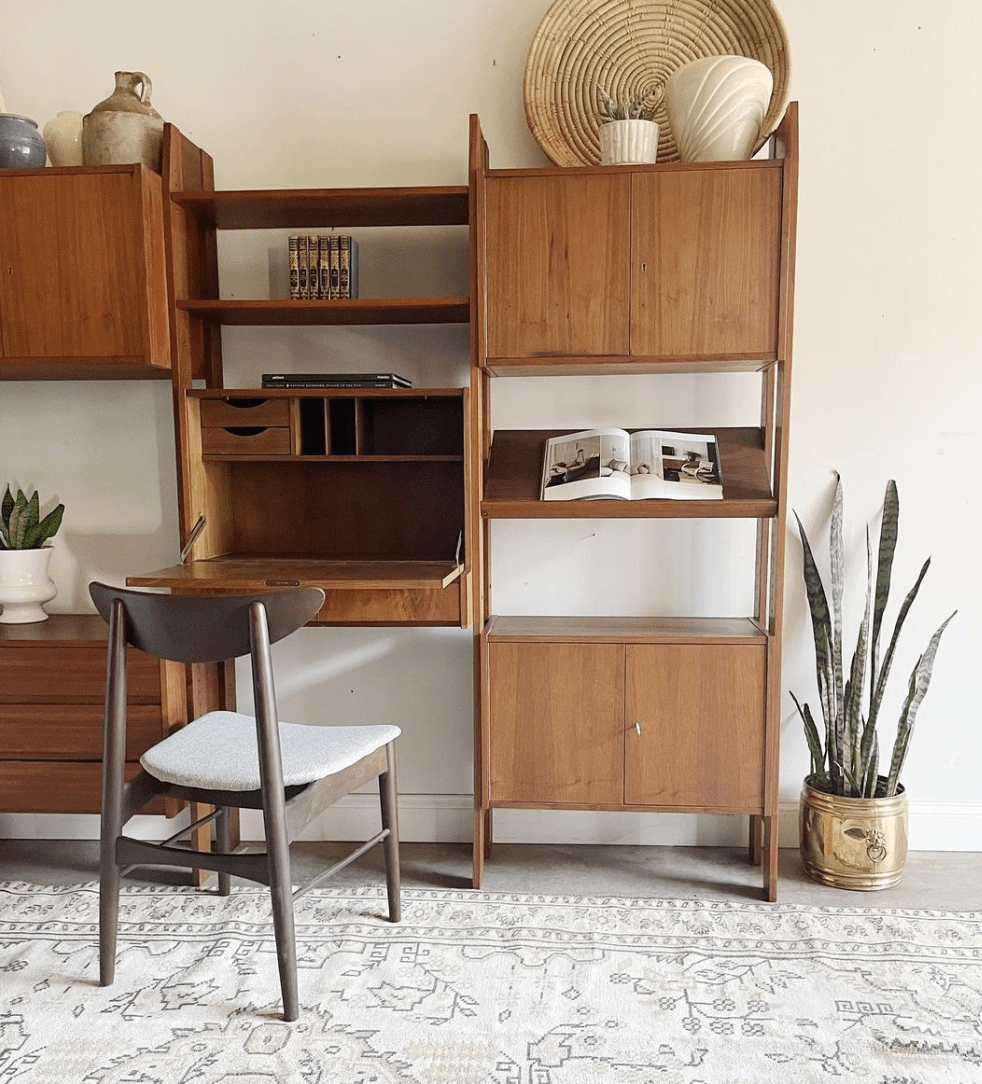mid century modern fold down desk with book chair and rattan basket vases and jugs next to it a gold pot with snake plant