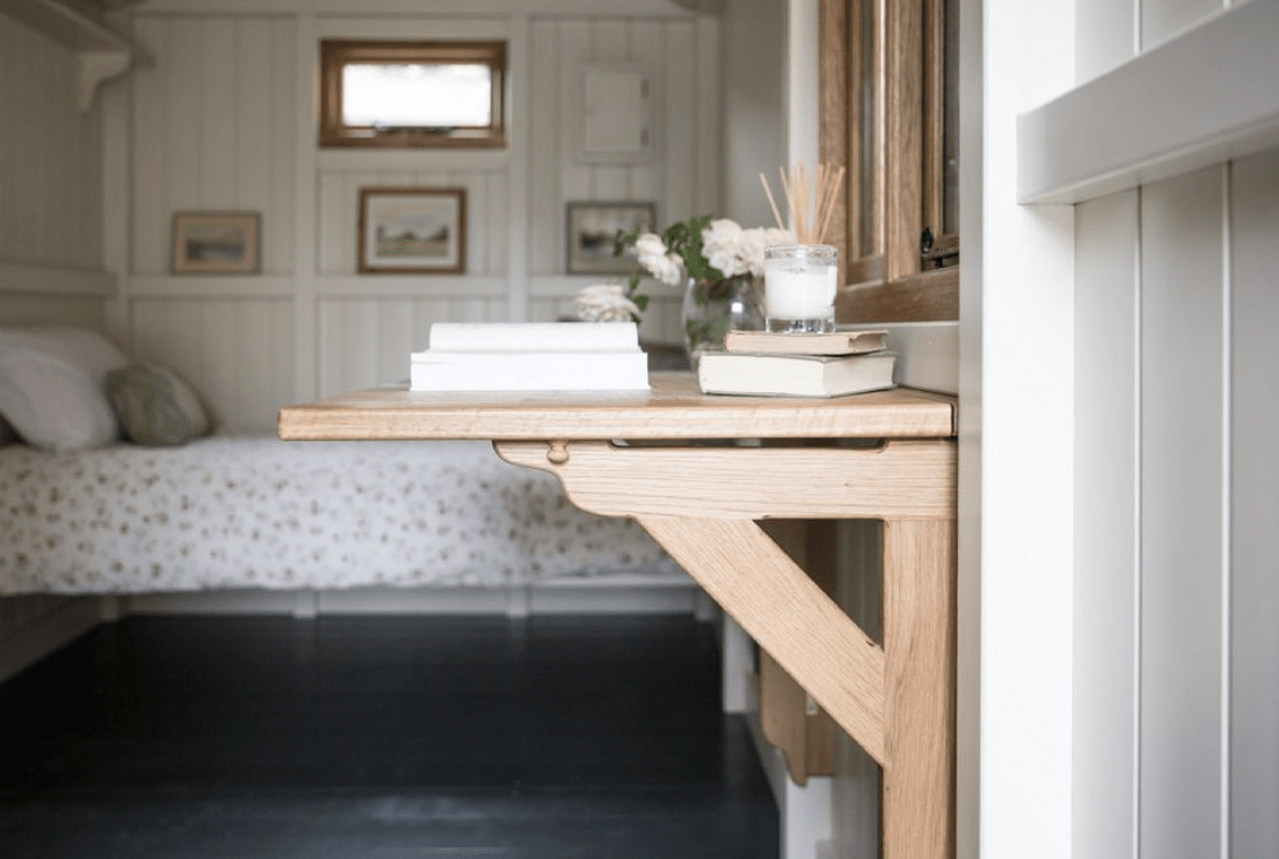 farmhouse style corbel fold down desk with books on top and in the background is a blurred bed and pictures on wall