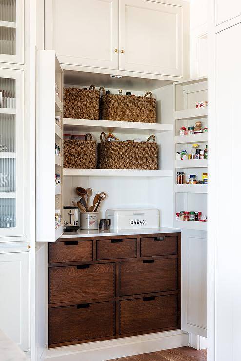 Cottage style kitchen features pantry cabinets accented with spice shelves on cabinet doors as well as brown wooden vegetable drawers.