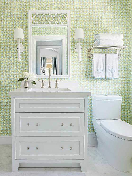 white vanity toilet over the toilet towel rack white mirror and wall sconces green pattern wallpaper
