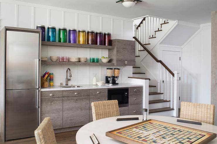 Basement kitchenette designed with floor to ceiling board and batten walls, a cereal station and a round white game table with wicker game chairs.