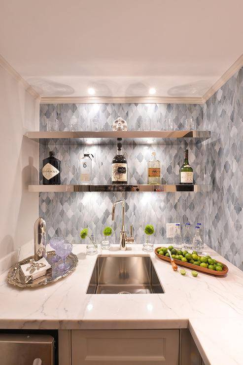 Wet bar nook boasts stainless steel floating shelves mounted on blue Moroccan style tiles over a gray polished marble countertop.