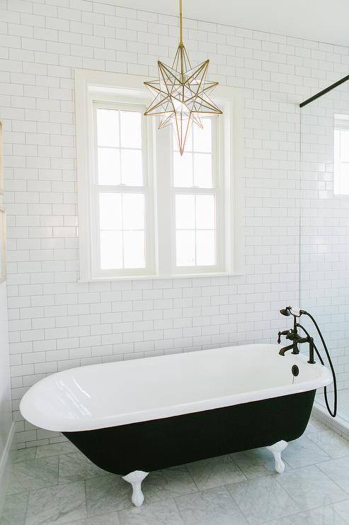 Black and white bathroom features walls lined with white subway tiles alongside a brass and glass star pendant, Pottery Barn Glass Star Pendant, illuminating a black claw foot tub paired with an oil rubbed bronze tub filler next to a seamless glass shower.