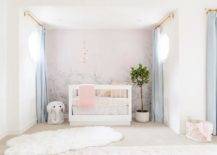 Nursery features a pink floral mural on accent wall with a gold mobile sits over a white wooden nursery crib with animal print bedding, baby blue curtains, a white wicker elephant hamper and a large white faux fur rug.