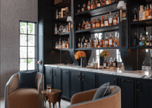 black wet bar with club chairs in front marble countertop tall shelves with liquor