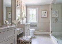 Elegant white master bathroom boasts light taupe wainscot walls and an animal print vanity stool placed at a marble top drop-down makeup vanity flanked by white washstands with marble countertops.