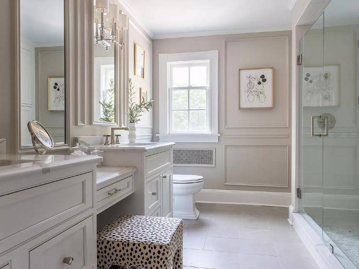 Elegant white master bathroom boasts light taupe wainscot walls and an animal print vanity stool placed at a marble top drop-down makeup vanity flanked by white washstands with marble countertops.