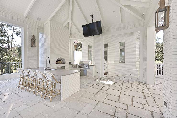 White French bistro stools at a concrete top island are featured in a Spacious covered patio with a white brick outdoor kitchen and custom pizza oven.