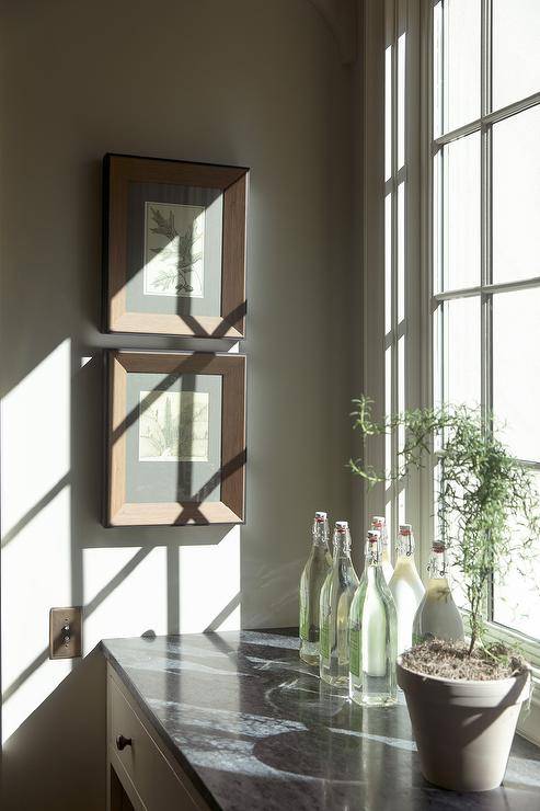 A black marble countertop is fixed beneath a pantry window and under stacked brown wood framed art.