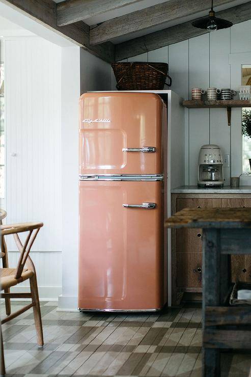 Peach vintage big chill refrigerator in a cottage kitchen boasting gray check floors, vaulted ceilings with beams.
