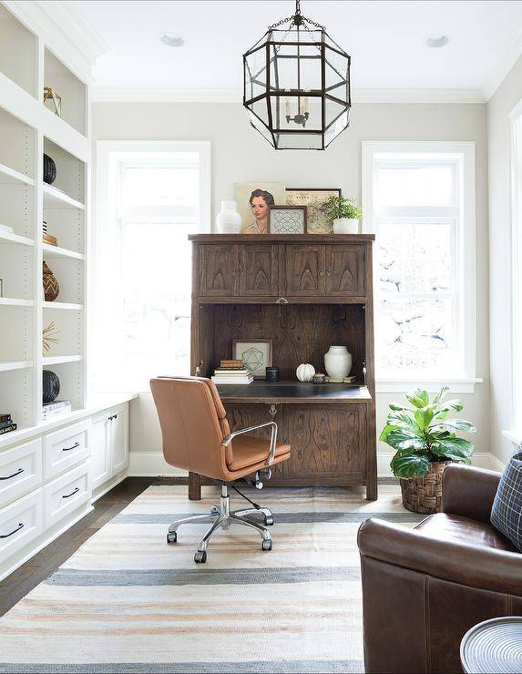 home office styled with walnut pulled down desk with leather chair on wheels rug ornate glass chandelier and white bookcase