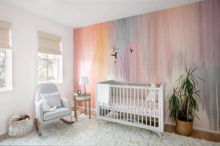 Nursery features a gray crib on a pink accent wall and a light gray rocker on a white shag rug.