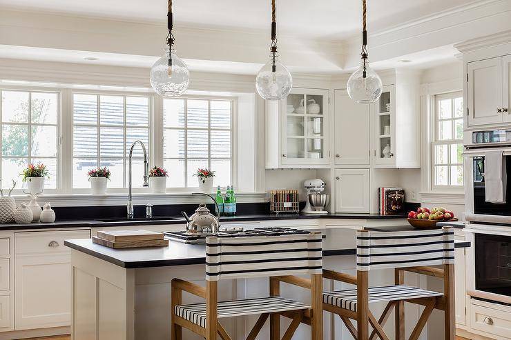 Two black stripe directors stool sit at a white kitchen island contrasted with a black quartz countertop lit by seeded glass lanterns.