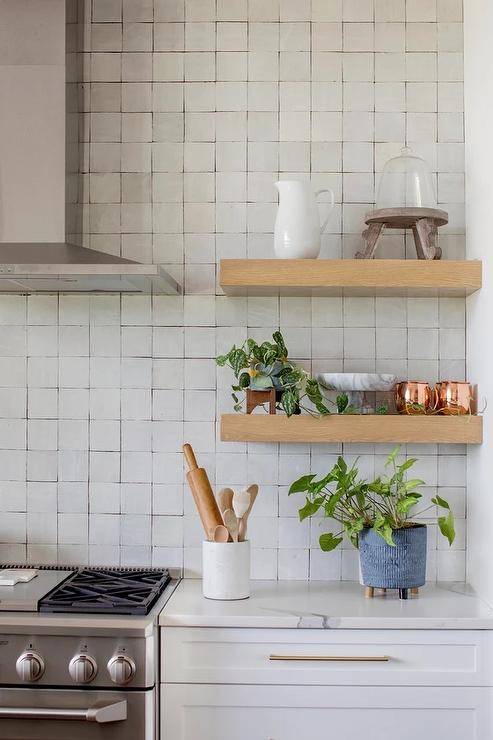 Stacked brown kitchen cabinets flank a black range hood mounted to white  subway backsplash tiles over a stai…