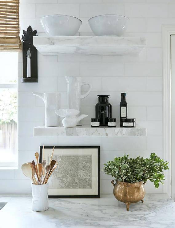 Marble floating shelves are stacked against white subway backsplash tiles and over a marble countertop.