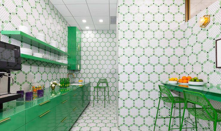 Stylish white and green kitchenette is clad in white and green hexagon backsplash tiles fixed behind glossy green floating shelves mounted beside stacked green lacquer cabinets and over green lacquer lower cabinets finished with a glossy green countertop.