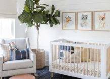A fiddle leaf fig sits on a blue jute rug in a stunning nursery boasting a white rocker topped with blue and beige pillows and paired with a round brown leather pouf. Baby animal art hangs from shiplap trim over a two-tone vintage style crib.