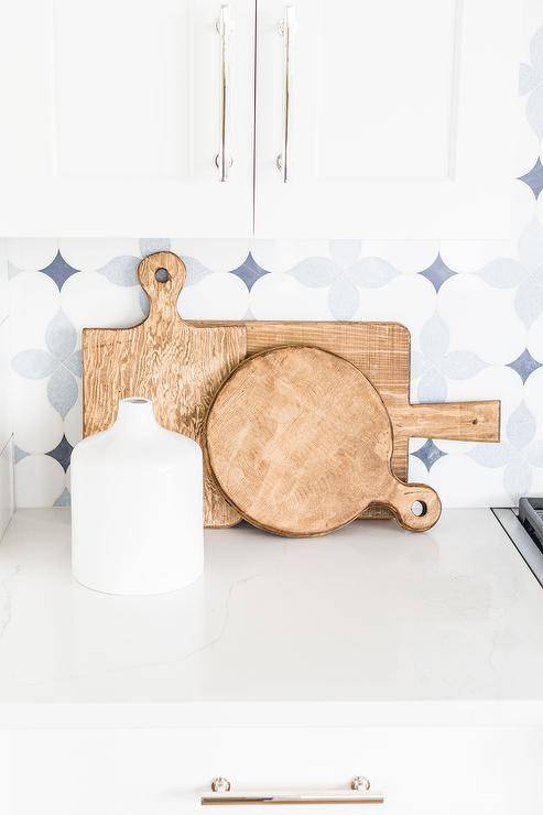 White kitchen cabinets topped with a white quartz countertop are fixed against Eveningstar Marble Tiles and beneath white upper cabinets finished with chrome pulls.