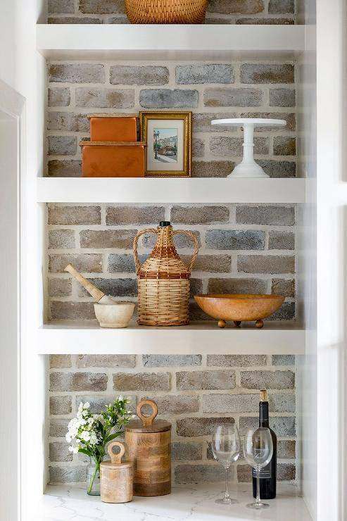 Cottage style kitchen finished with faded red brick backsplash, white shelves and styled decor.