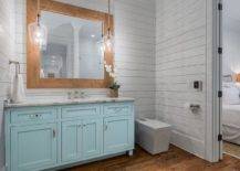 Rustic glass and rope lights over a turquoise blue bath vanity with a white marble top. White shiplap walls offer a cottage feel surrounding stained oak hardwood floors complimenting a wood framed vanity mirror.