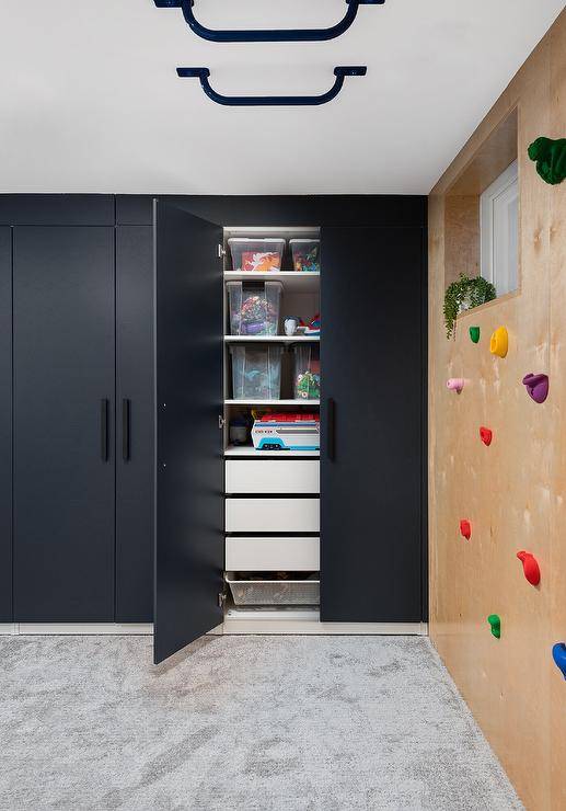 Contemporary basement playroom boasts a gray rug placed beneath a rubber rock climbing wall and in front of black closet doors with matte black hardware.