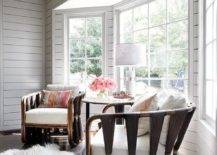 A white sheepksin rug sits in front of gray rope and wood lounge chairs placed on a stained wood floor in front of pay windows framed by gray shiplap.