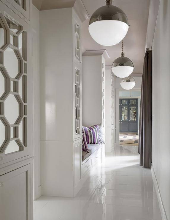 Contemporary hallway features a built-in bench lined with a gray cushion and purple and gray striped pillows flanked by floor to ceiling geometric mirrored cabinets illuminated by Hicks Pendants.