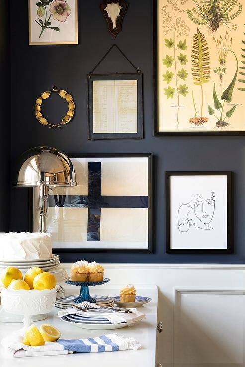 A black dining room wall is accented with an eclectic art gallery hung over white wainscoting.