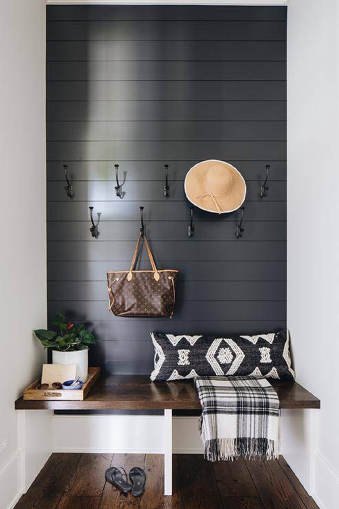 Mudroom bench designed in a floating oak feature with a black shiplap wall and iron hooks. Styled decor adds a charming touch to the overall built-in bench.