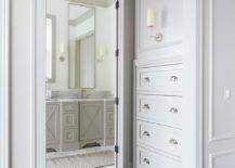 A Ziyi Sconce mounted to a gray wainscot wall illuminates light gray built-in hallway drawers accented with polished nickel cup pulls. The hallway leads to an en suite master bathroom.