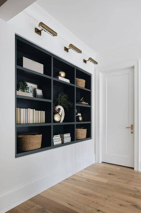 Hallway features black niche shelves illuminated by antique brass picture lights.
