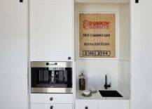 Cottage kitchen features a built-in coffee station hidden by sliding barn doors on rails. A vintage Dunkin donuts sign decorates the built-in finished with a sink, an oil rubbed bronze faucet, a wold built-in coffee machine, and white shaker cabinets. Oil rubbed bronze hardware stand out against the white finished cabinetry keeping a black and white theme consistent.