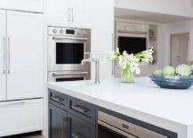 White quartz waterfall countertop on a black center island fitted with a ample cabinet space and drawers featuring a built-in microwave.