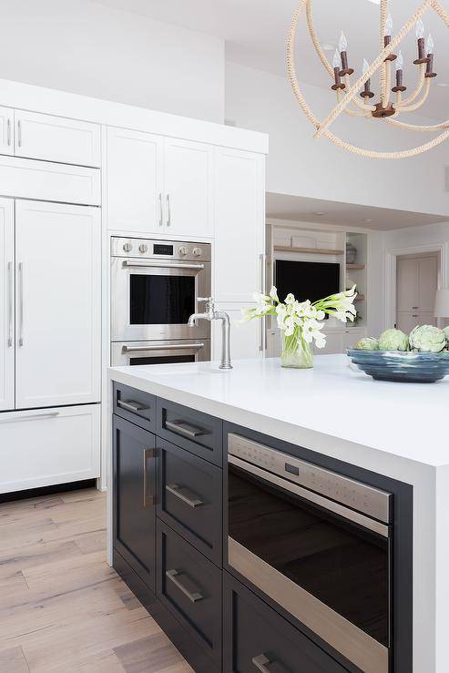 White quartz waterfall countertop on a black center island fitted with a ample cabinet space and drawers featuring a built-in microwave.