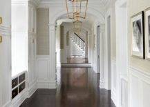 long hallway with gold chandeliers white trim wainscotting and dark walnut floors