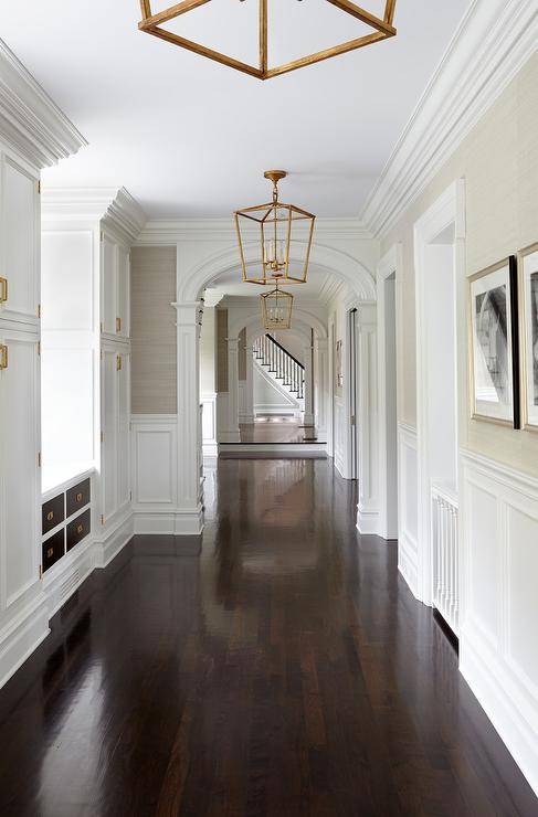 long hallway with gold chandeliers white trim wainscotting and dark walnut floors