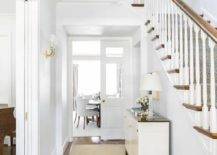 Hallway features a white and brown cabinet over a cream runner on a white staircase wall.