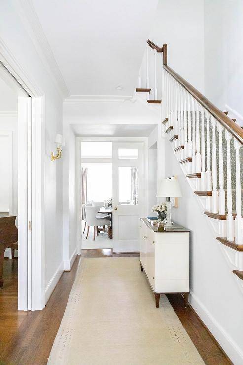 Hallway features a white and brown cabinet over a cream runner on a white staircase wall.