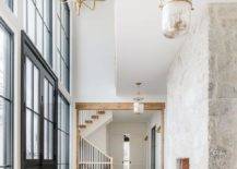 Cottage style foyer features a tall rustic gray stone fireplace and blond herringbone wood floors, illuminated by a mercury glass lantern.