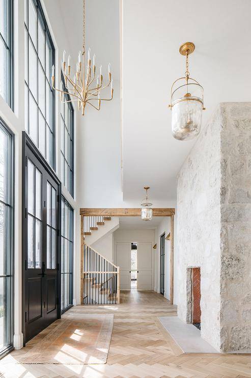 Cottage style foyer features a tall rustic gray stone fireplace and blond herringbone wood floors, illuminated by a mercury glass lantern.